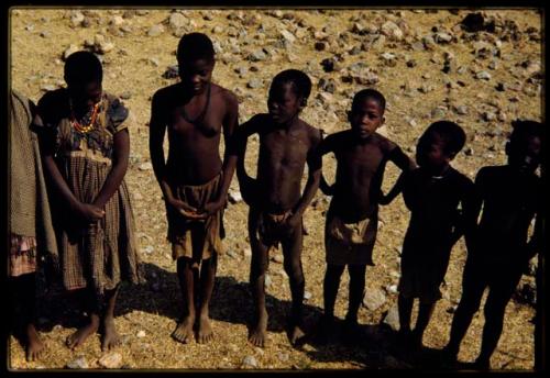 Group of people standing, including a girl wearing a red dress, view from the expedition truck