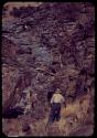 Laurence Marshall and another expedition member, with view of rocky side of cliff and water source at Scho-Scho gulch