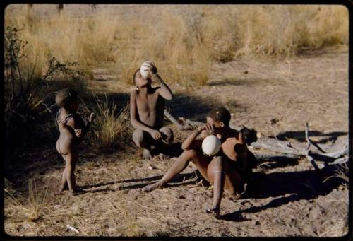 Children, Eating: Two young people drinking from ostrich egg shells, with a child standing beside them