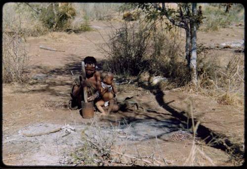 Children, Mothers nursing babies: !Ungka (sister of ≠Toma) pounding something in a mortar, with her daughter, Sa≠gai, sitting on her leg