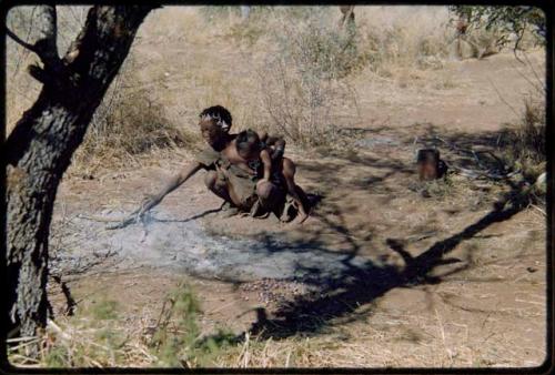 Children, Mothers nursing babies: !Ungka (sister of ≠Toma) cooking something in a fire, with her daughter, Sa≠gai, sitting on her leg