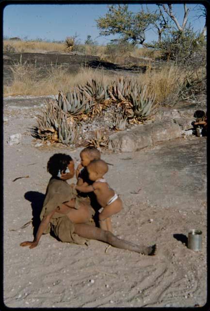 Children, Mothers nursing babies: !Ungka (sister of Toma) sitting, with her daughter, Sa≠gai, and !Ungka Norna standing next to her; aloes in the background