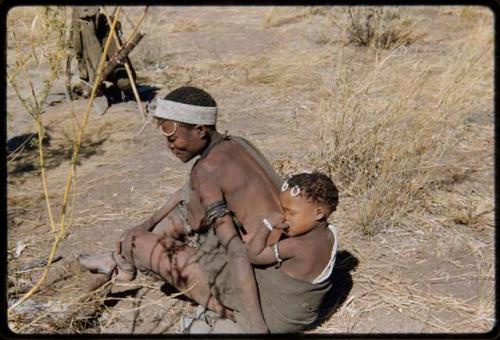 Children, Carrying: Wife of "Gao Hunchback" (headman of Band 11) wearing an ostrich eggshell bead headband, sitting with a child tied to her back