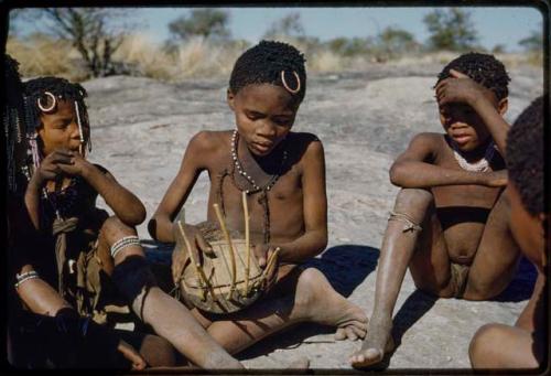 Music: Boy playing a //guashi, with a boy and girl sitting next to him