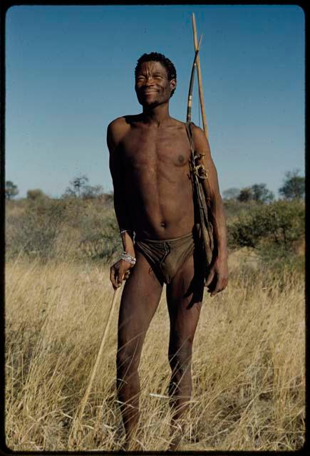 Portraits: /Ti!kay standing, with his hunting bag over his shoulder