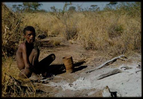 Portraits: "Old /Gishay" sitting next to the ashes of a fire, with a wooden container on the ground next to him