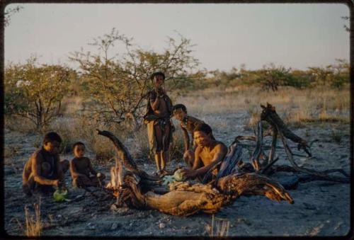 Wood: ≠Toma and "Gao Medicine" eating with a group of people next to a fire, with two girls standing next to them