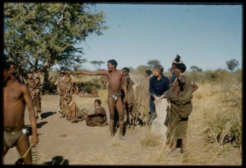 Expedition, Groups: "Gao Medicine" standing and pointing, with other people sitting and standing near him, receiving rations from Lorna Marshall and Kernel Ledimo