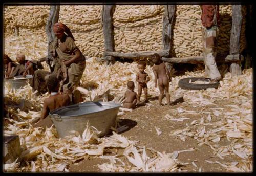 Expedition, Metzger: Women husking corn, with children standing and sitting near them