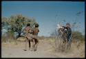 Expedition, Photography: Two boys carrying "Little ≠Gao" in a kaross, playing the "airplane game," with Lorna Marshall standing near them holding her helmet over a camera lens