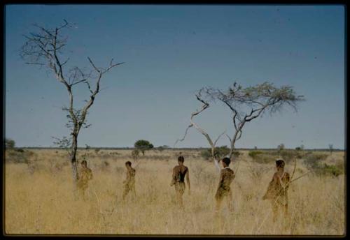 Five hunters walking through grass in a line