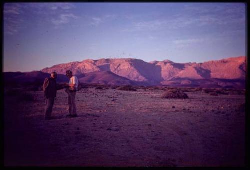 Scenery, Mountains: Two expedition members standing, with mountains in the background, in early evening light