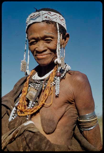 Ornament: /Gam wearing many ornaments, including a headband, cowrie shells, rectangular bead ornaments, beads around her neck and upper arm bracelets