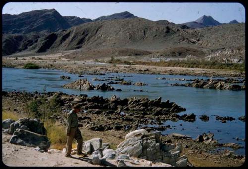 Charles Koch walking along the Kunene River, with hills in the background