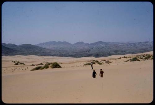 Men walking on sand dunes, with mountains in the distance