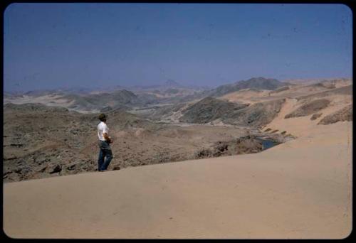 Kurt Ahrens standing at edge of a sand dune, looking east at the Kunene River