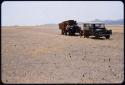 Expedition trucks (Dodge and Land Rover) driving across a flat plain