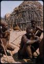 Three men sitting in front of a hut, close-up