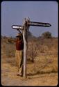 Philip Hameva standing under a signpost and pointing toward "Ondangua" (Ondangwa)