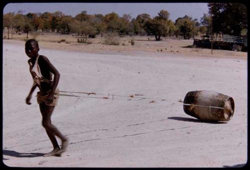 Boy pulling a barrel of water across a road, close-up