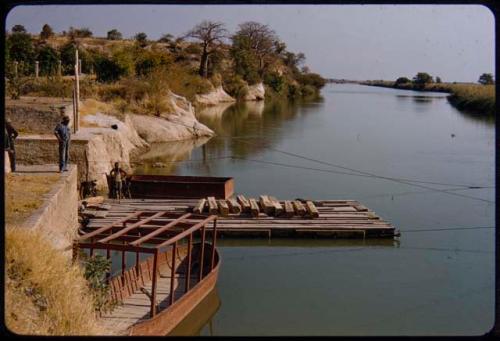 Men loading a pont on the Kunene River, with other men standing nearby watching