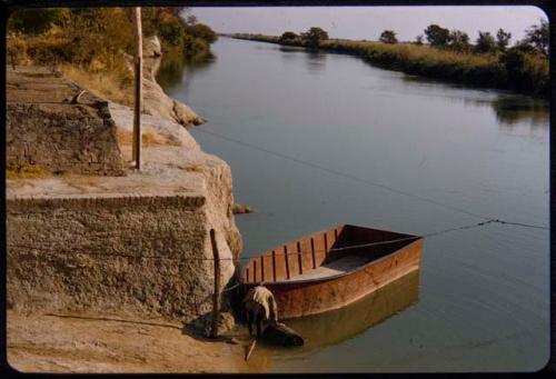 Man filling a barrel with river water next to a boat