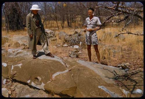 Mr. Prinsloo and Nicolaas Jacobus van Warmelo standing on a rock with a petroglyph on Mr. Prinsloo's farm