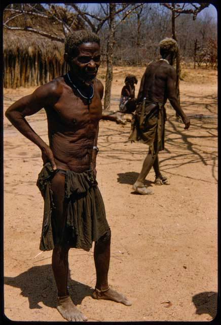 Man standing, with another man walking behind him