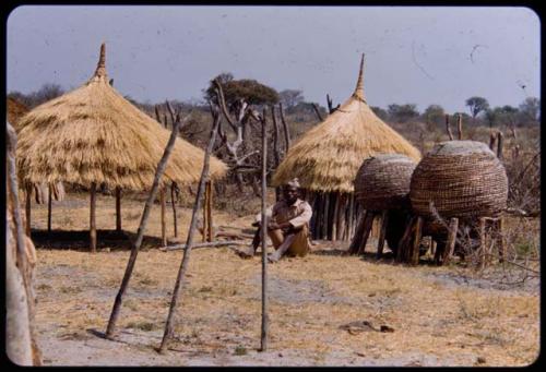 Man sitting next to huts and storage baskets