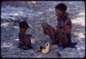 Hambia's wife and child sitting, with a gourd pipe on the ground next to them