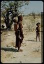 Woman carrying a child, with another child standing next to her wearing a hat