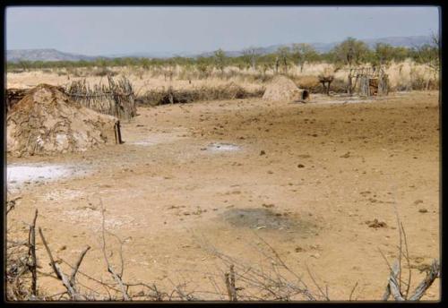 Mud-plastered huts, part of a brush fence and cleared space