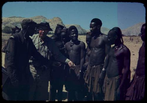 Group of men standing with Laurence Marshall and Edward Hartley (the expedition interpreter and guide), looking at a Polaroid print of themselves