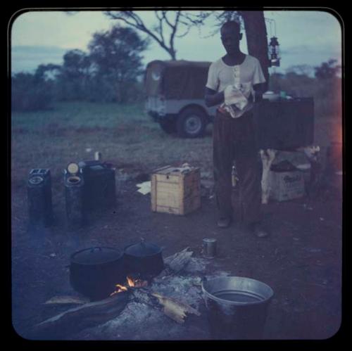 Louis standing by fire and pots, with a truck in the background