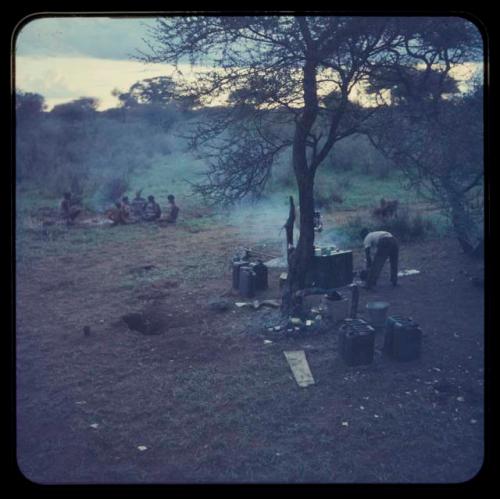 Louis cooking at the expedition camp, with a group of people sitting in the background