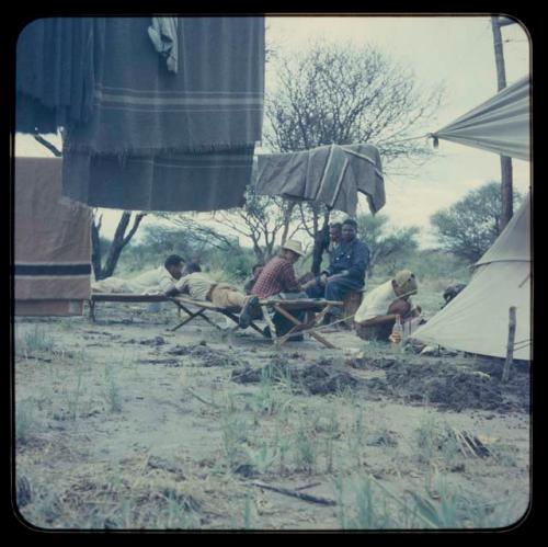 Expedition members, including Lorna Marshall, gathered at their camp, with tents, blankets, and cots in the background