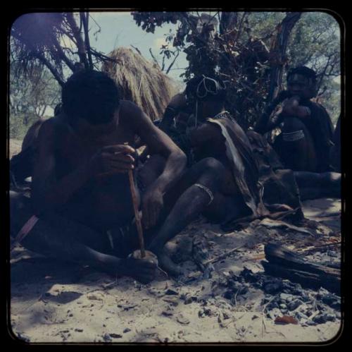 Bo Jo sitting and poisoning an arrow, with other people sitting behind him