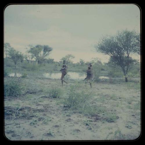 Two women walking, carrying children 
