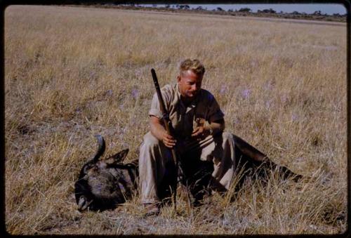 Theunis Berger sitting on a dead wildebeest, holding a gun