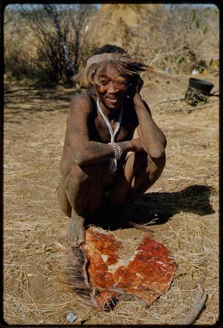 Scraping Skin: Bo wearing a badger cap, with a small skin on the ground in front of him