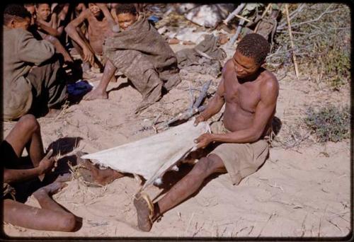 Scraping Skin: Man sitting with a skin tied to his toes, pulling on it to stretch it