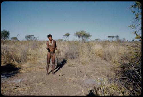 Spring Hare: "Old Gau" wearing white beads, standing and holding a springhare prodder