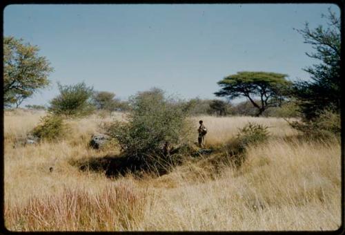 Water: Woman with a baby tied to her back and a child standing near a small, unused waterhole at Gautscha