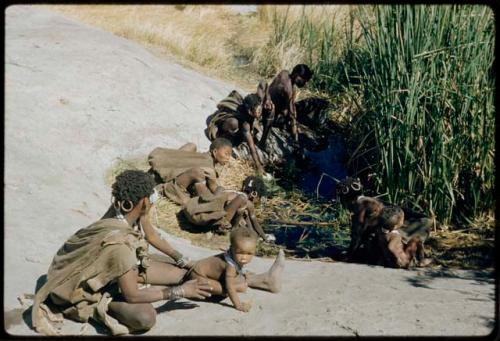 Water: !U sitting with !Ungka Norna and other women and children at the Gautscha waterhole, with !Ungka leaning over the water