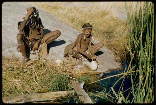 Water: Bau (daughter of Ti!kay) filling an ostrich eggshell with a tortoise shell dipper, with another woman sitting next to her