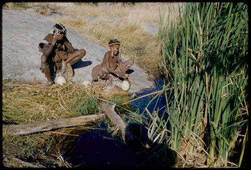 Water: Bau (daughter of Ti!kay) filling an ostrich eggshell with a tortoise shell dipper, with another woman sitting next to her