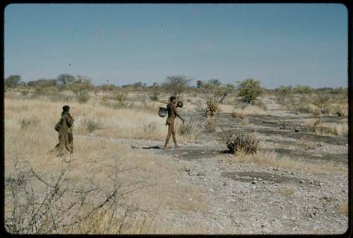 Water: "/Qui Navel" carrying an Ovambo pot on a stick, walking with a woman to a waterhole