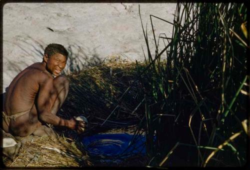 Water Hole: "Old Gau" sitting at a waterhole, filling an ostrich eggshell with water