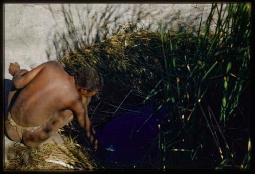 Water Hole: "Old Gau" sitting at a waterhole, filling an ostrich eggshell with water by submerging it