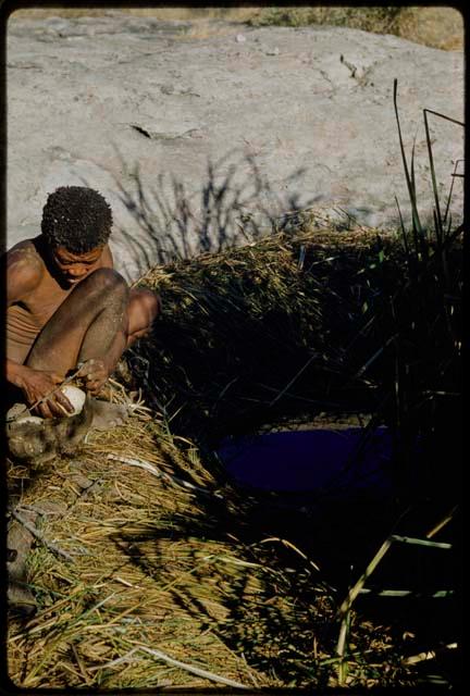 Water Hole: "Old Gau" sitting at a waterhole, putting an ostrich eggshell into his bag